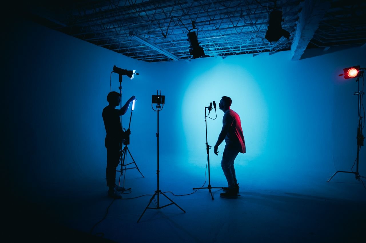 Silhouetted artists in a studio with dramatic lighting setup and microphone.